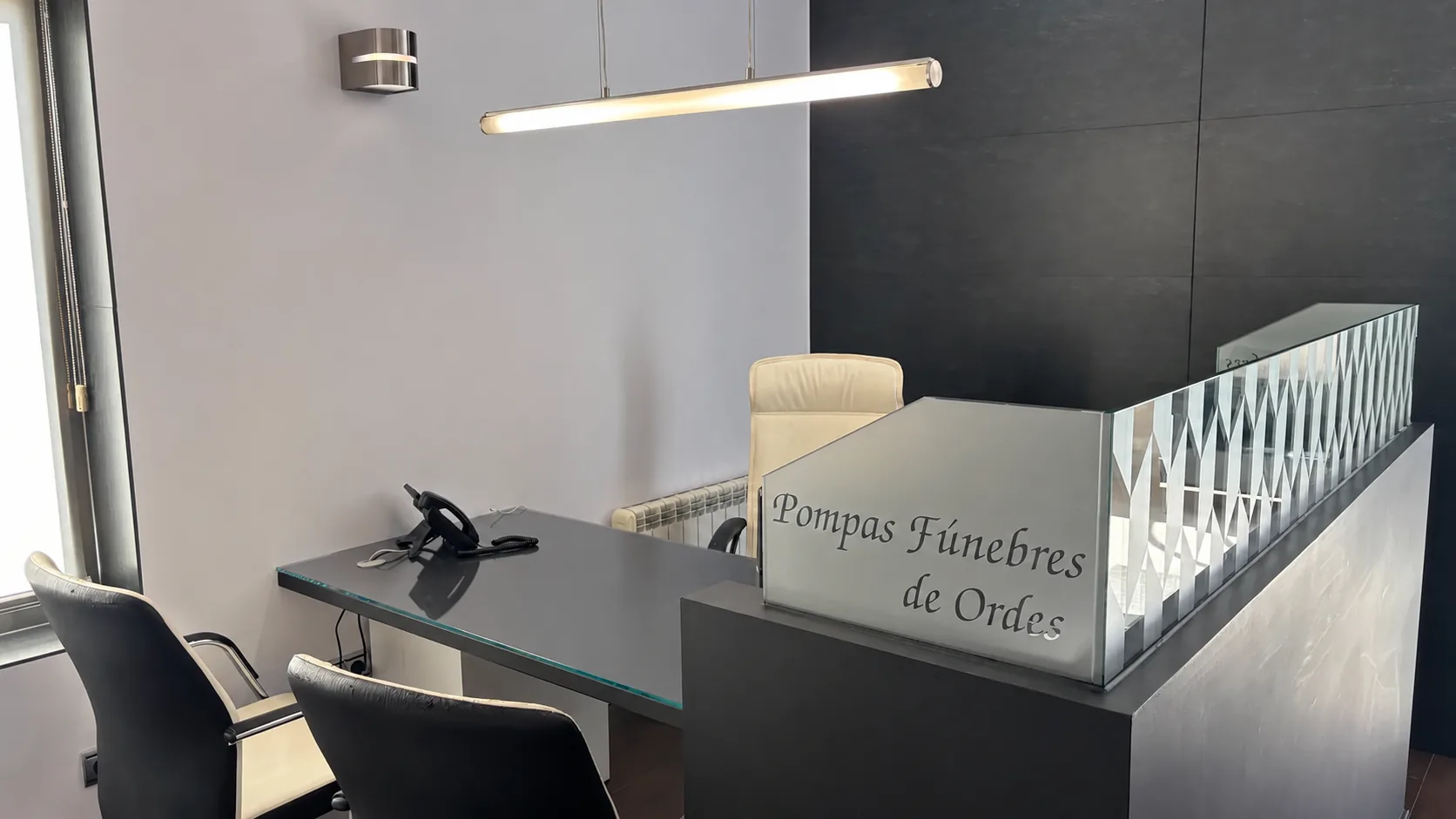 Despacho de atención de la oficina, con la mesa de trabajo, dos sillas para las familias y el mostrador con el nombre de la empresa