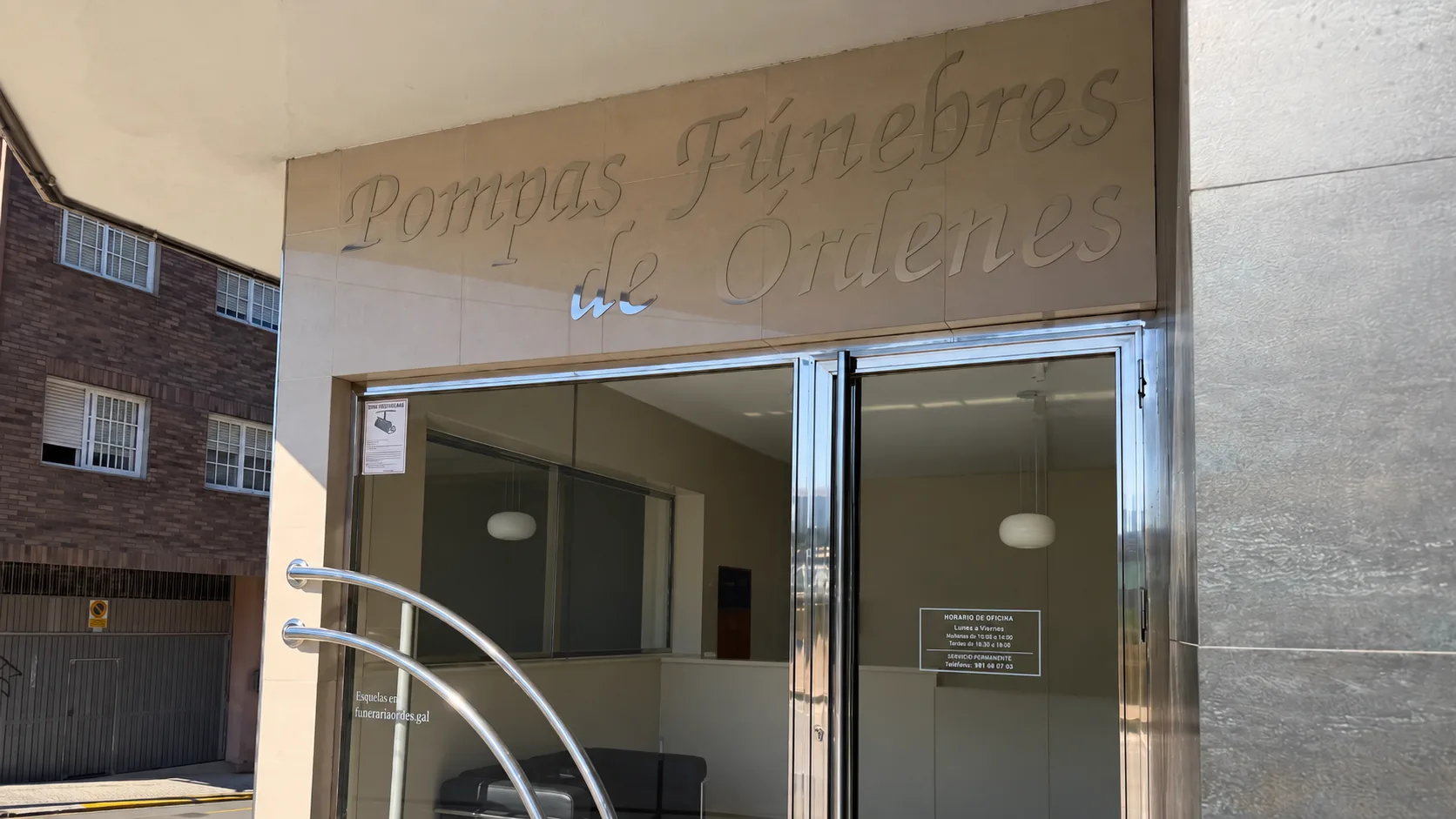 Entrada de la oficina de Pompas Fúnebres en Rúa Campeiras, con el rótulo «Pompas Fúnebres de Órdenes» sobre la puerta de cristal