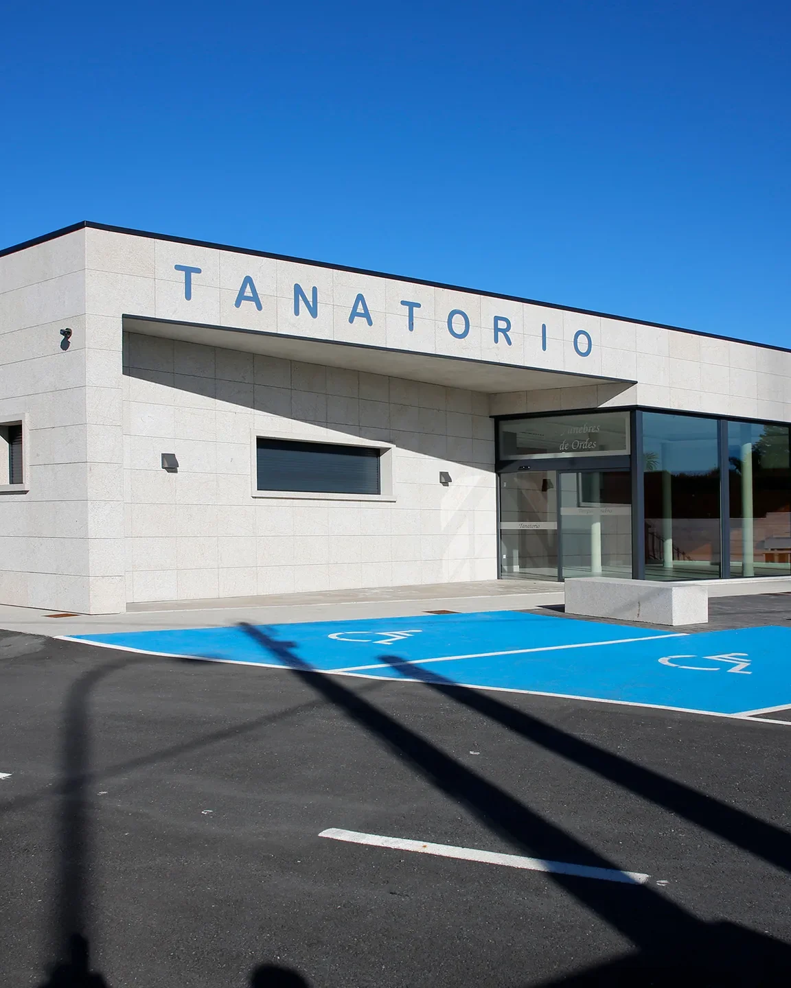 Fachada del Tanatorio do Mesón do Vento con el rótulo «TANATORIO», el acceso acristalado y las plazas de aparcamiento para movilidad reducida